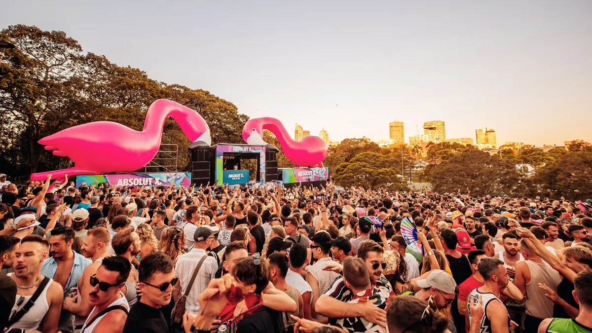 A packed daytime crowd in Victoria Park at Fair Day, with inflatable flamingos above the stage.