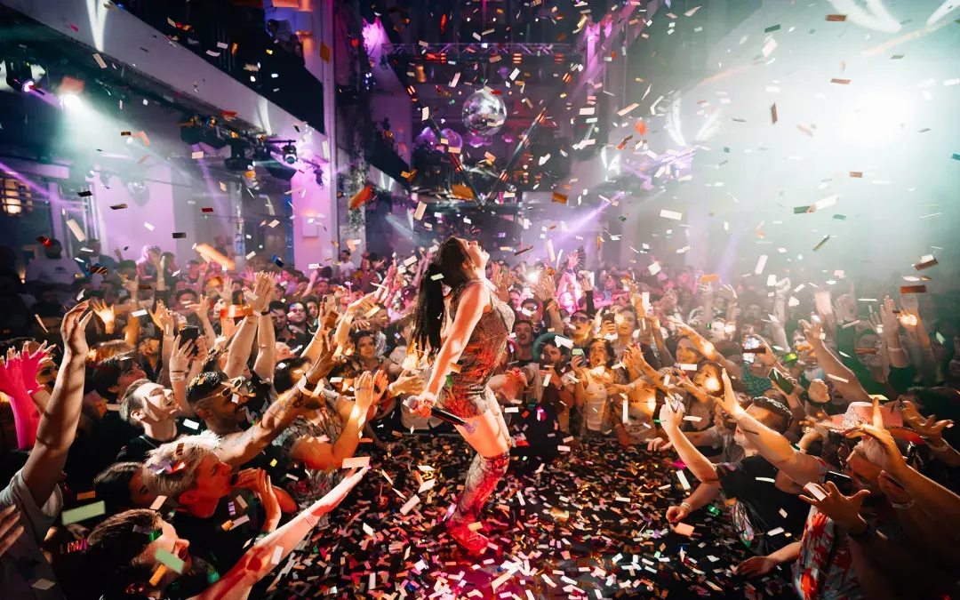 A packed dancefloor under confetti, with a performer on the stage.